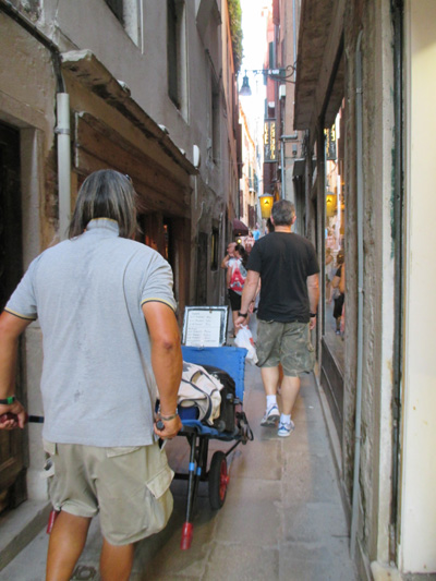 3 photos show a man with shoulder-length gray hair and wearing shorts pushing a cart through crowded plazas and alley.